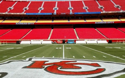 Campo do Arrowhead Stadium Campo do Arrowhead Stadium, casa do Kansas City Chiefs, com logo da equipe pintado no gramado, visto de um ângulo central com assentos vermelhos ao fundo.